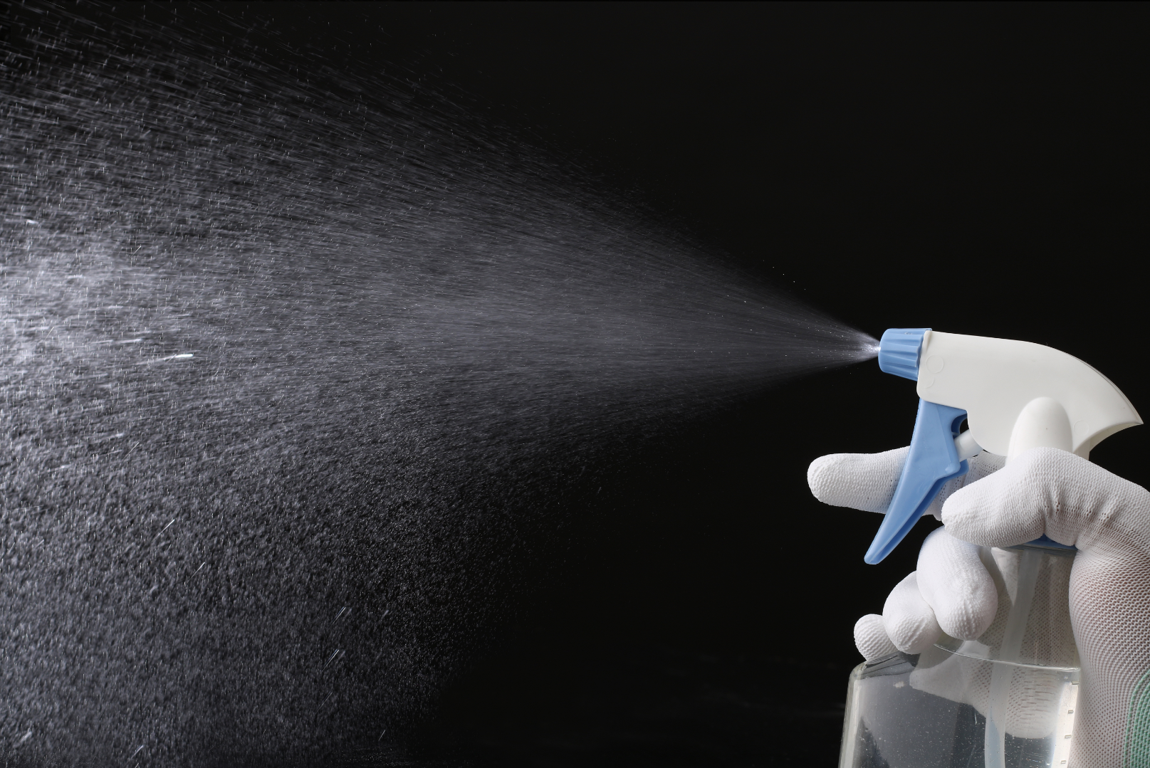 spray bottle being sprayed by a gloved hand on a black background